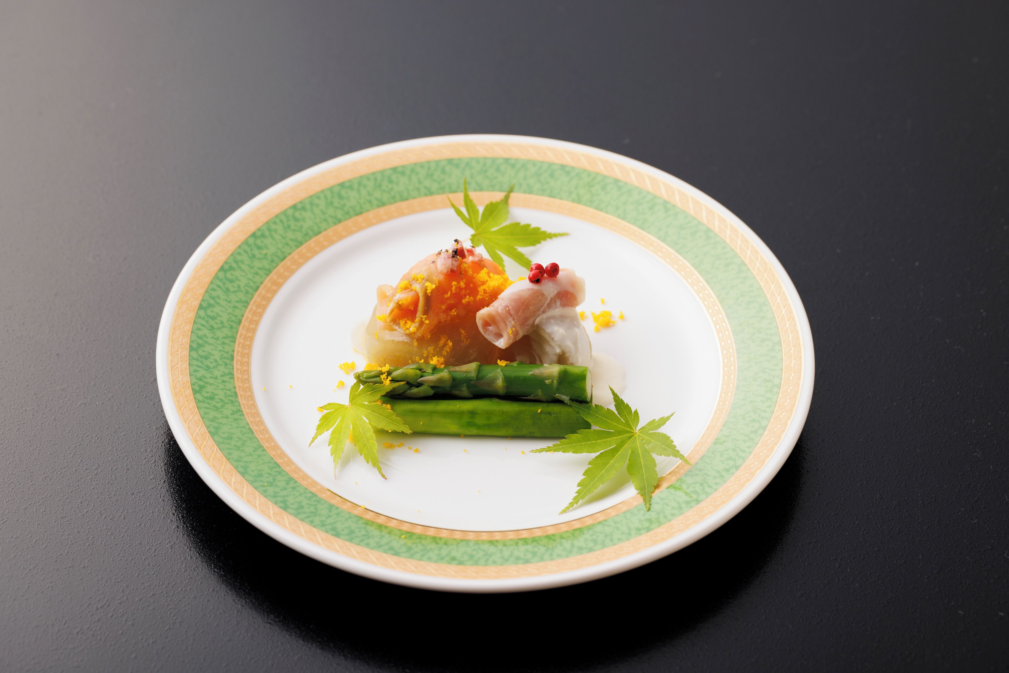 A plate with a piece of fish, asparagus, and garnishes on a dark surface.