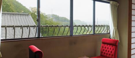 A room with a large window, two red upholstered chairs, and a small wooden table.