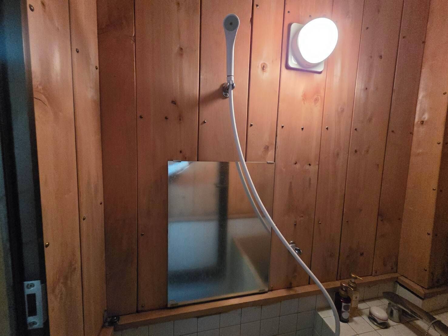 Baño de cabaña de madera con ducha, espejo y lámpara.
