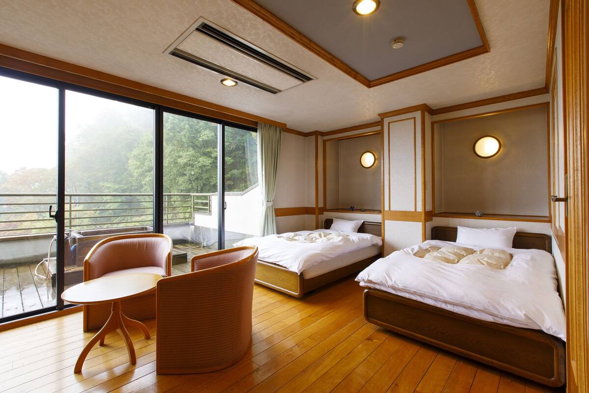 Habitación de hotel con dos camas, un balcón con una silla y una mesa.