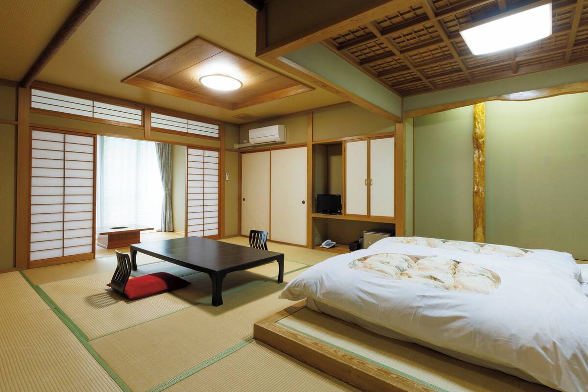 Una habitación tradicional japonesa con suelo de tatami, una mesa baja, una cama y puertas correderas.