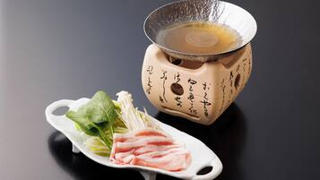Jogo de chá japonês tradicional com bule e xícara de cerâmica, acompanhados de um prato de cerâmica branco com carne e legumes fatiados.