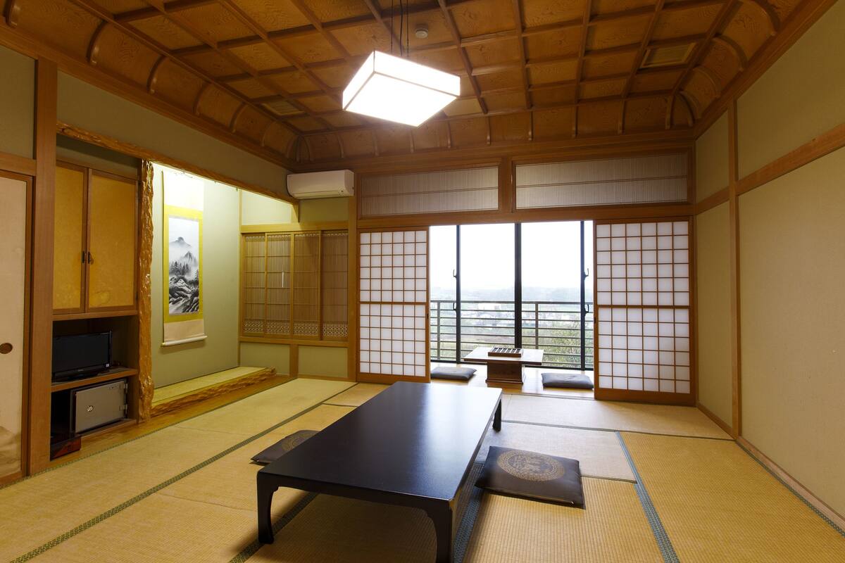 Una habitación japonesa tradicional con suelo de tatami, una mesa baja, puertas correderas y vistas a través de biombos shoji.