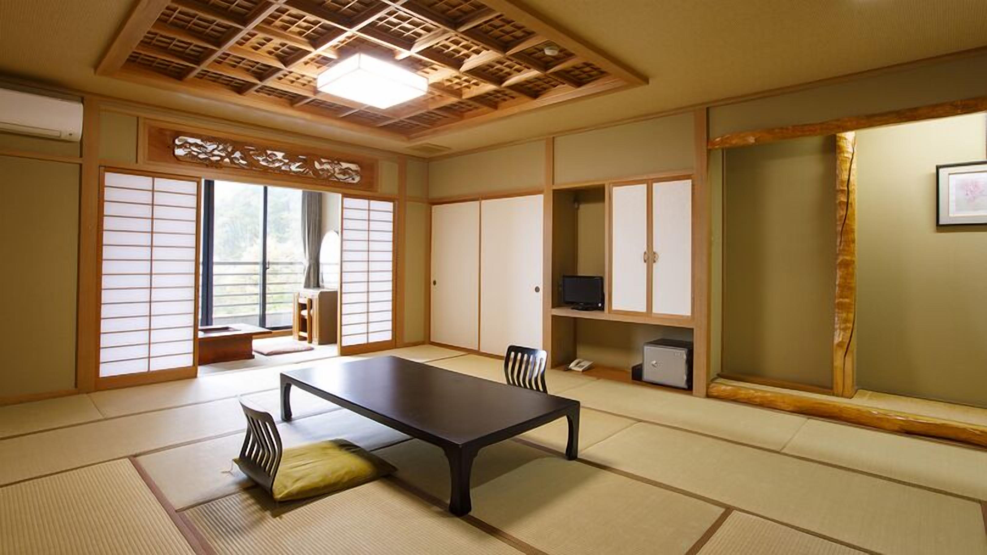 Une pièce de style japonais traditionnel, avec un sol recouvert de tatamis, une table basse, des portes coulissantes et un téléviseur.