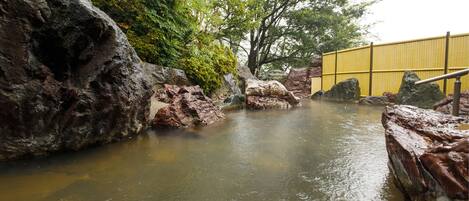 A natural hot spring area with large rocks and a yellow fence.