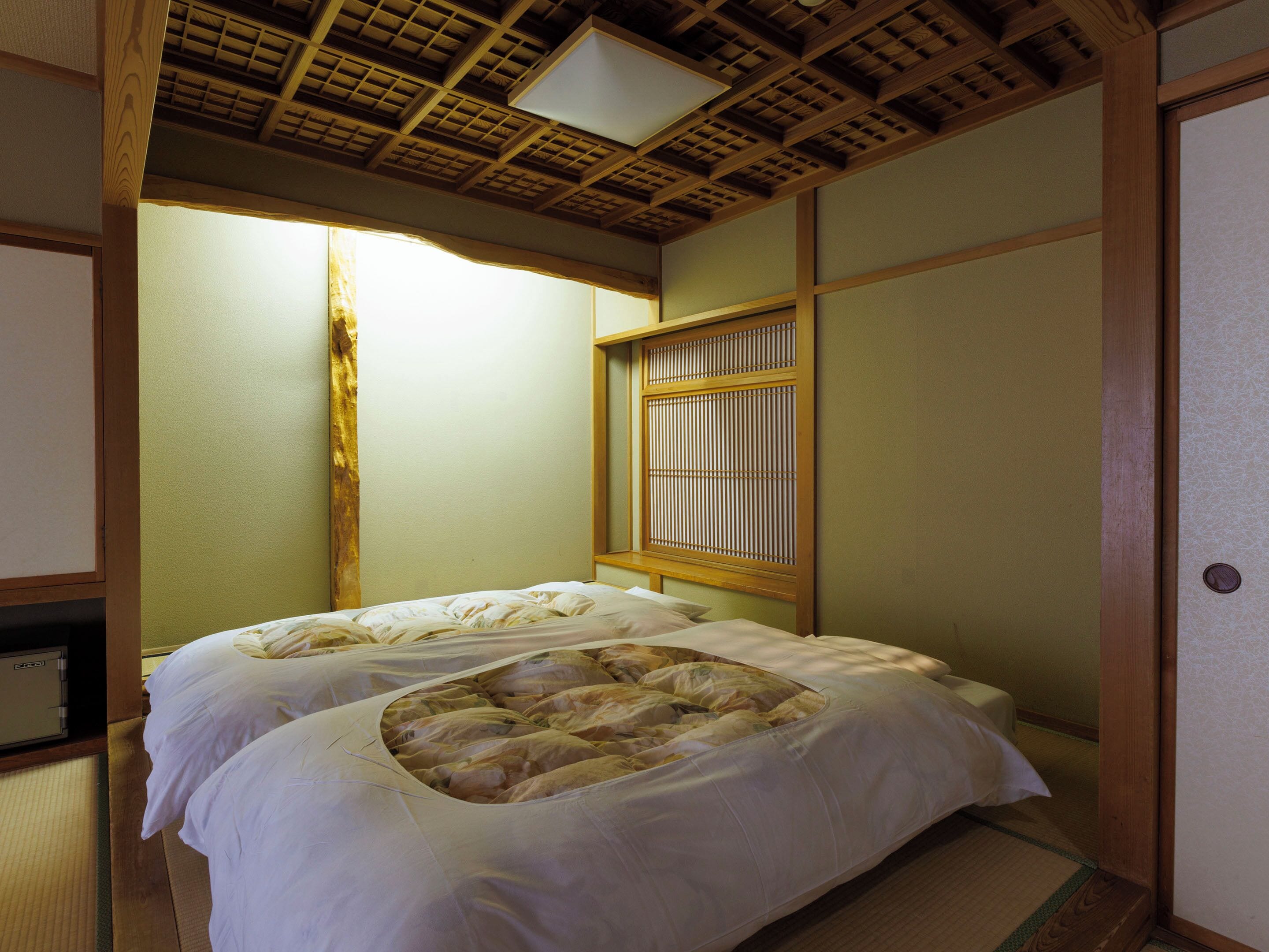 A traditional Japanese-style room with tatami flooring, a low wooden bed with a futon, a shoji screen, and a sliding door.