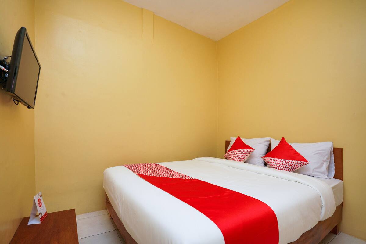 A hotel room with a bed, a TV mounted on the wall, and a wooden nightstand.
