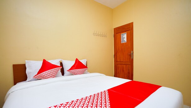 A hotel room with a bed, two pillows, a red and white bedspread, and a wooden door. - Hotel O Az Zahra Residence Syariah (Surabaya)