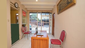 A reception area with a wooden desk, two red chairs, a clock, and a framed text on the wall. - Hotel O Az Zahra Residence Syariah (Surabaya)