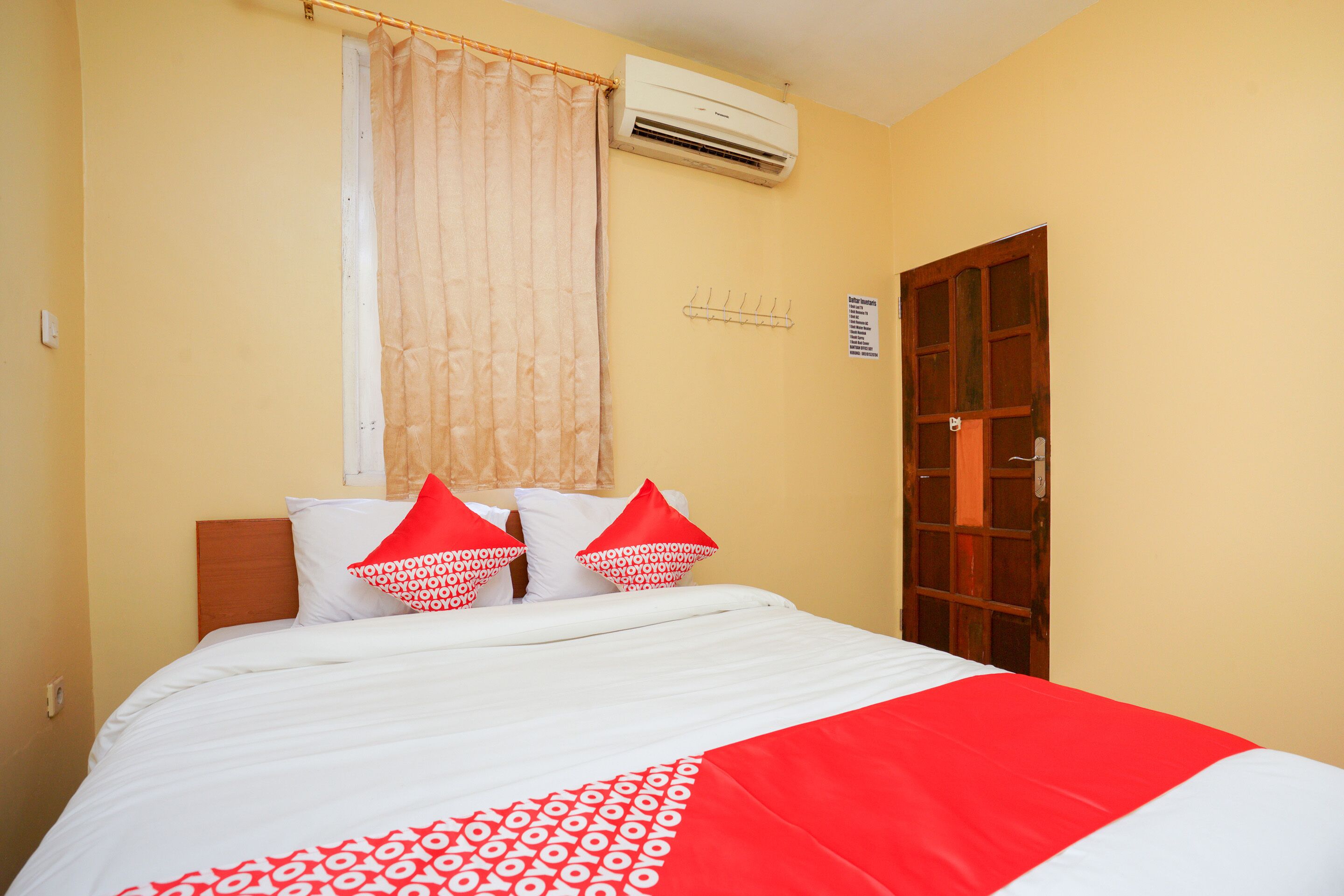 A hotel room with a bed, a window with a curtain, an air conditioning unit, and a door.