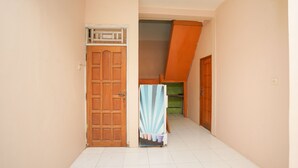 A narrow hallway with a wooden door, a small table with a striped tablecloth, and a staircase leading to an upper level. - Hotel O Az Zahra Residence Syariah (Surabaya)