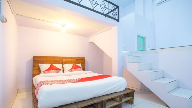 A bedroom with a wooden bed, white walls, and a staircase. - OYO 2415 Ibma Smart Syariah (Pandaan)