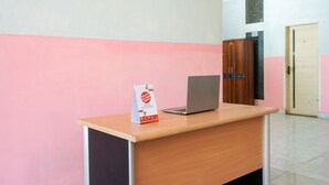 A reception desk with a laptop, a sign, and a wooden cabinet in a room with pink and white walls. - OYO 2415 Ibma Smart Syariah (Pandaan)