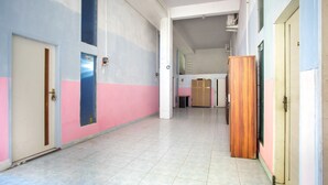 A corridor with doors on both sides, a tiled floor, and a wooden cabinet in the center. - OYO 2415 Ibma Smart Syariah (Pandaan)