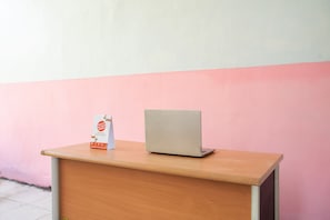 A wooden desk with a laptop and a brochure against a pink wall. - OYO 2415 Ibma Smart Syariah (Pandaan)