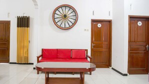 A room with a wooden table, a red sofa, a wall-mounted decorative wheel, and two wooden doors with numbers. - OYO 2718 Backpacker's Homestay Jlegong (Wonosobo)