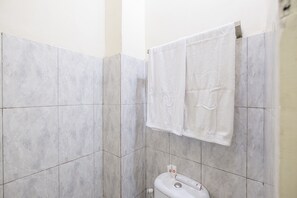 A bathroom with grey tiled walls, a white toilet, and two white towels hanging on a rack. - OYO 2718 Backpacker's Homestay Jlegong (Wonosobo)