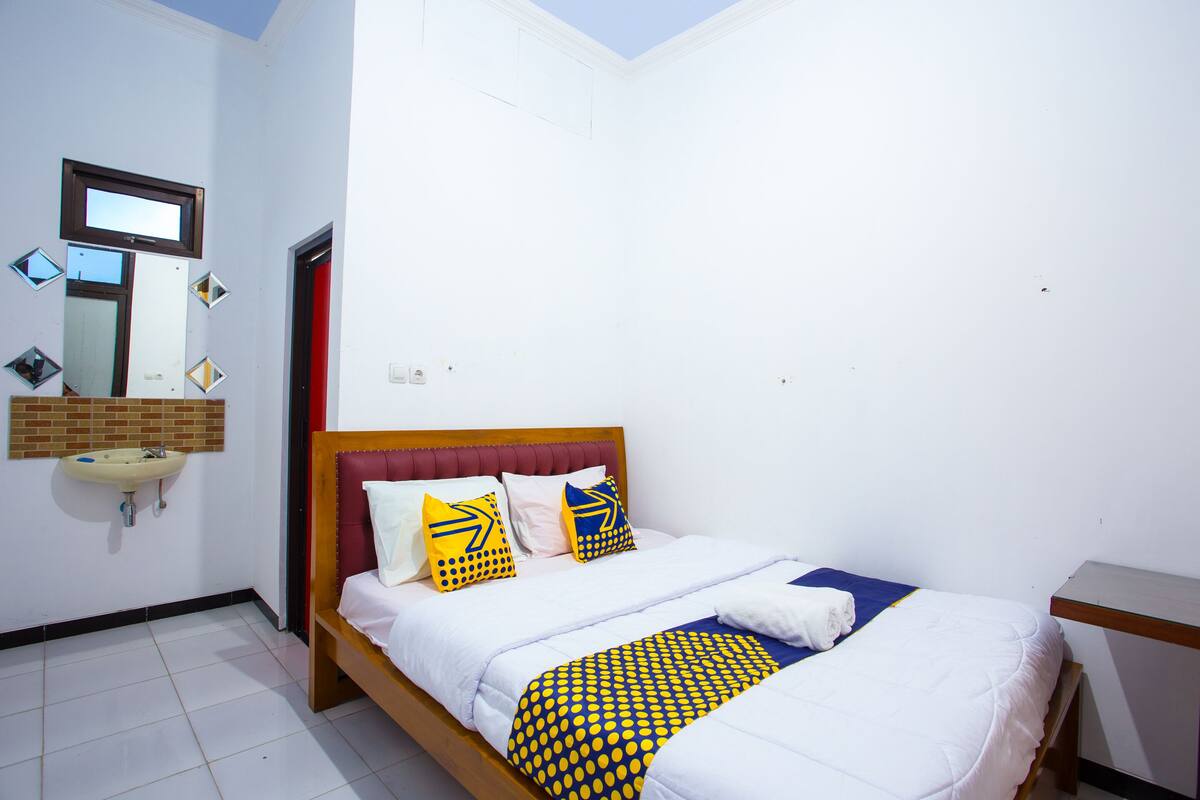 A bedroom with a bed, a bedside table, a mirror, and a sink.
