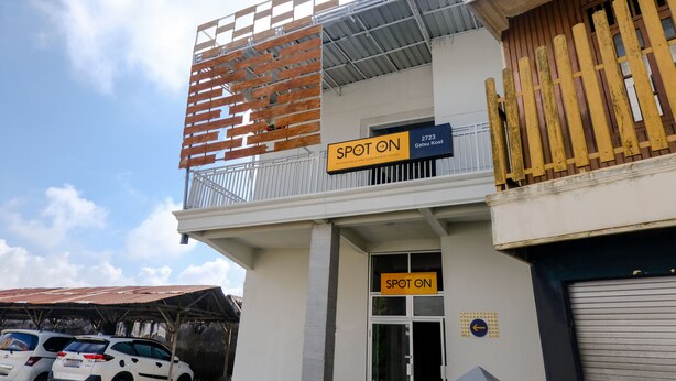 Un edificio con un letrero que dice 'SPOT ON', un balcón con baranda de madera y una puerta de garaje.