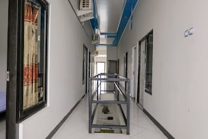 Un pasillo con barandilla de metal, ventanas amplias con cortinas y unidades de aire acondicionado.