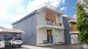 Un edificio con un letrero que dice 'SPOT ON', un balcón y una camioneta SUV blanca estacionada.