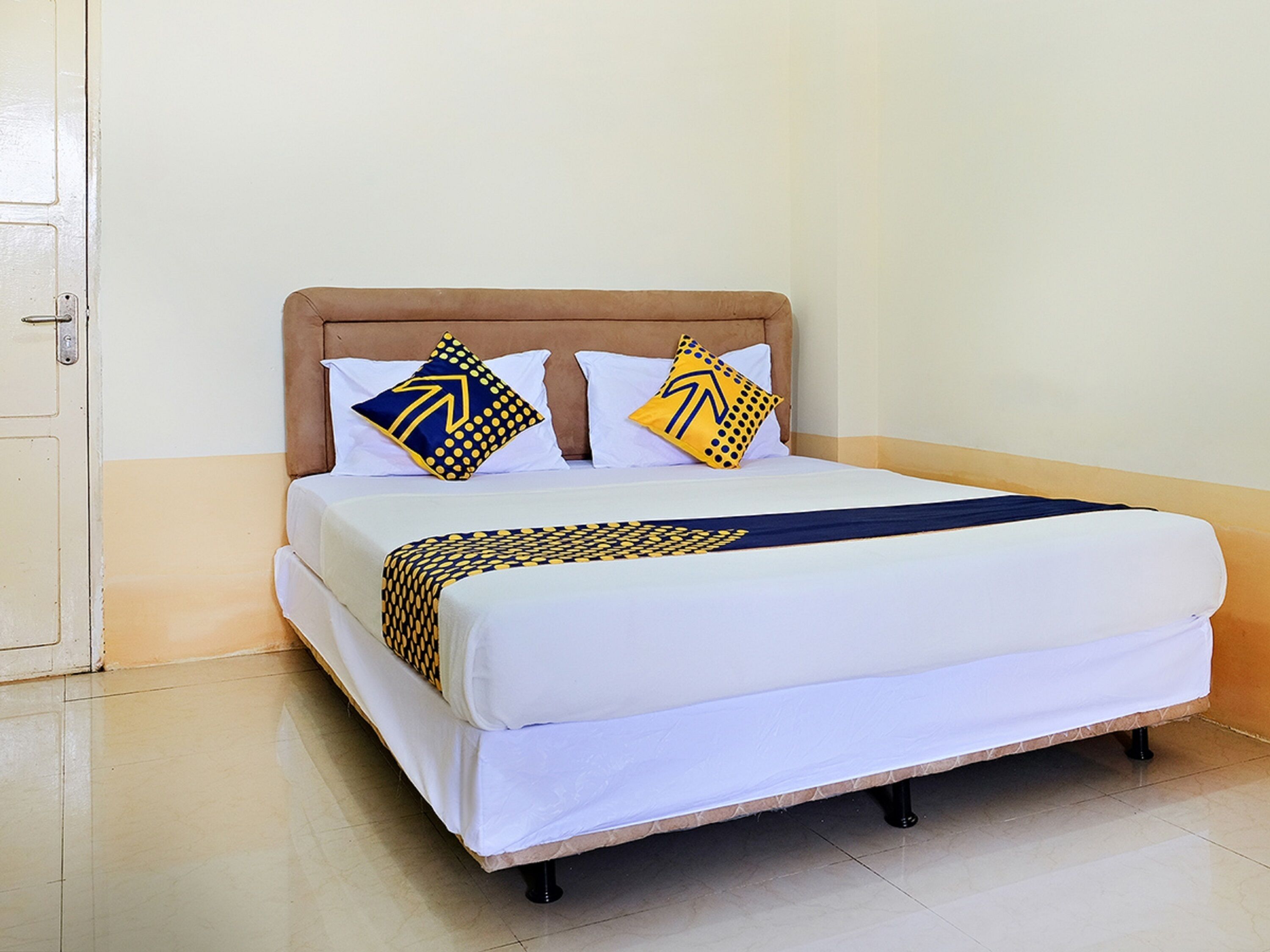 Un lit avec un matelas blanc, une tête de lit marron et deux oreillers à motifs géométriques.
