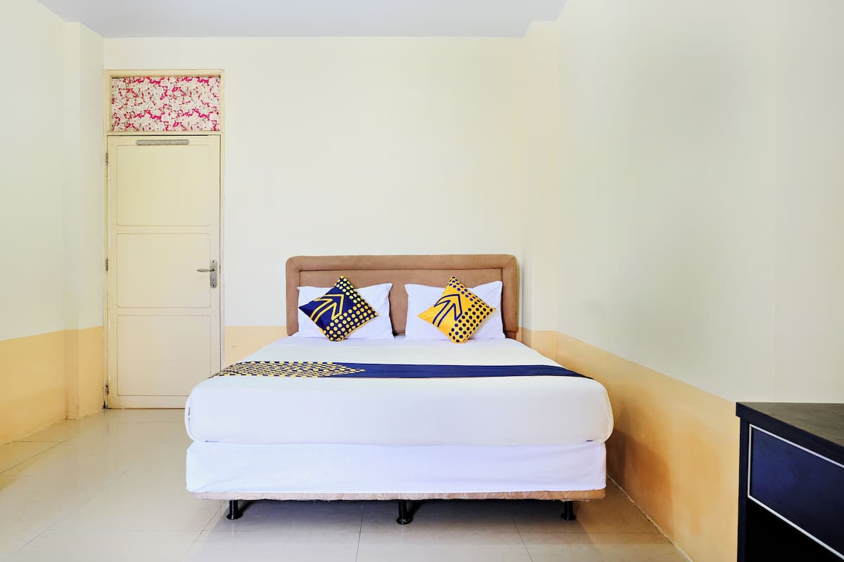 Un lit simple avec une tête de lit en bois, deux oreillers à motifs géométriques, une couvre-lit bleue et blanche, et une porte sobre ornée d’un motif floral sur sa partie supérieure.