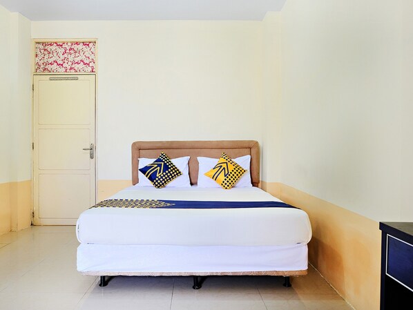 A single bed with a wooden headboard, two pillows with geometric patterns, and a white bedspread.