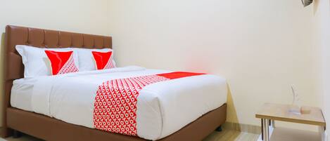 A neatly made bed with a brown headboard, white and red bedding, and a small bedside table with a lamp.