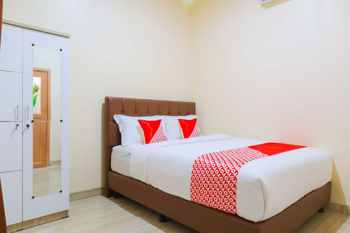 A neatly made bed with a brown headboard, white bedding, and red accents.
