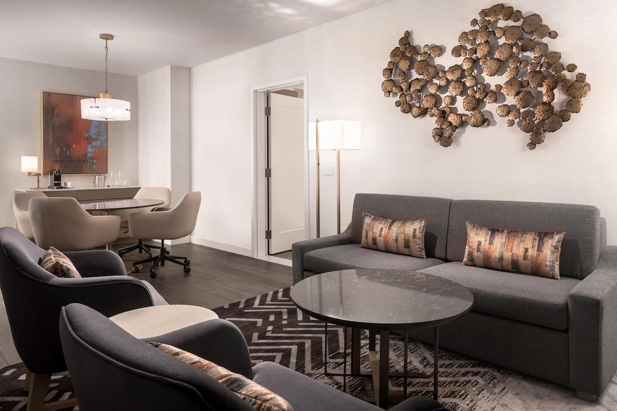 Una sala de estar moderna con un sofá gris, dos sillones, una mesa de centro y un comedor con una mesa y sillas.