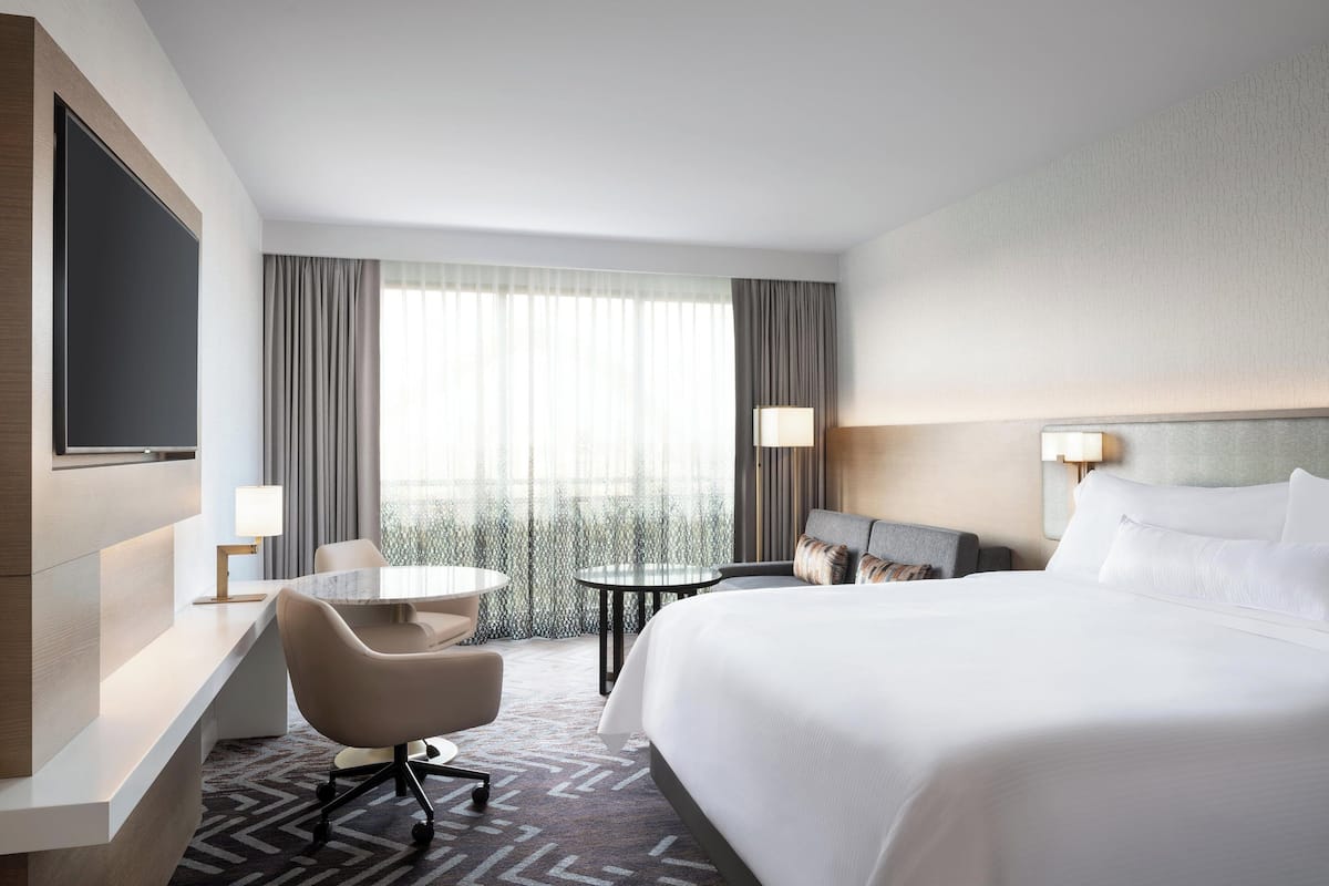 Habitación de hotel con una cama grande, un escritorio con silla, una pequeña mesa redonda y un televisor montado en la pared.