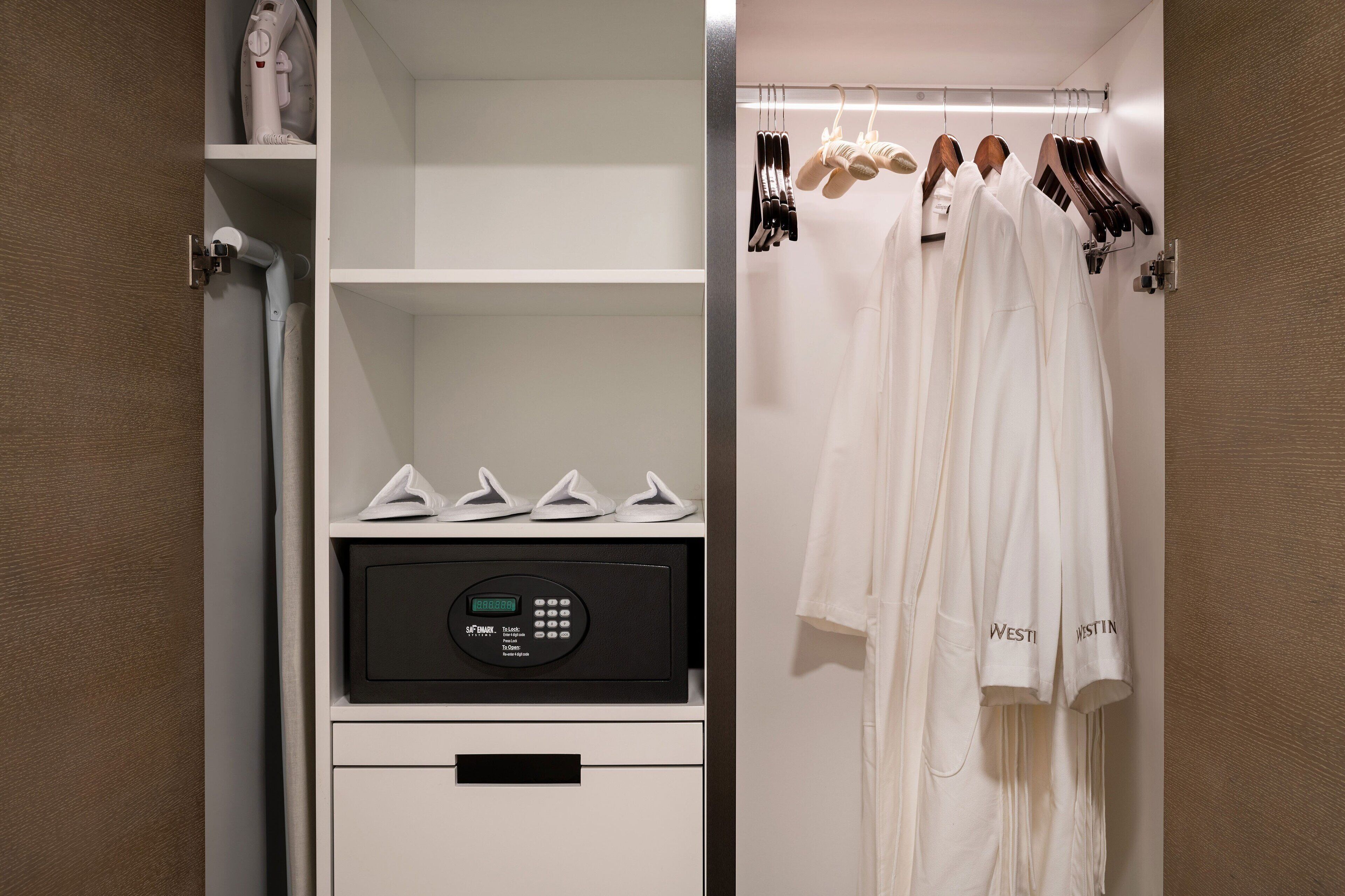 A hotel room with a white wardrobe, a control panel, and a rack of white robes.