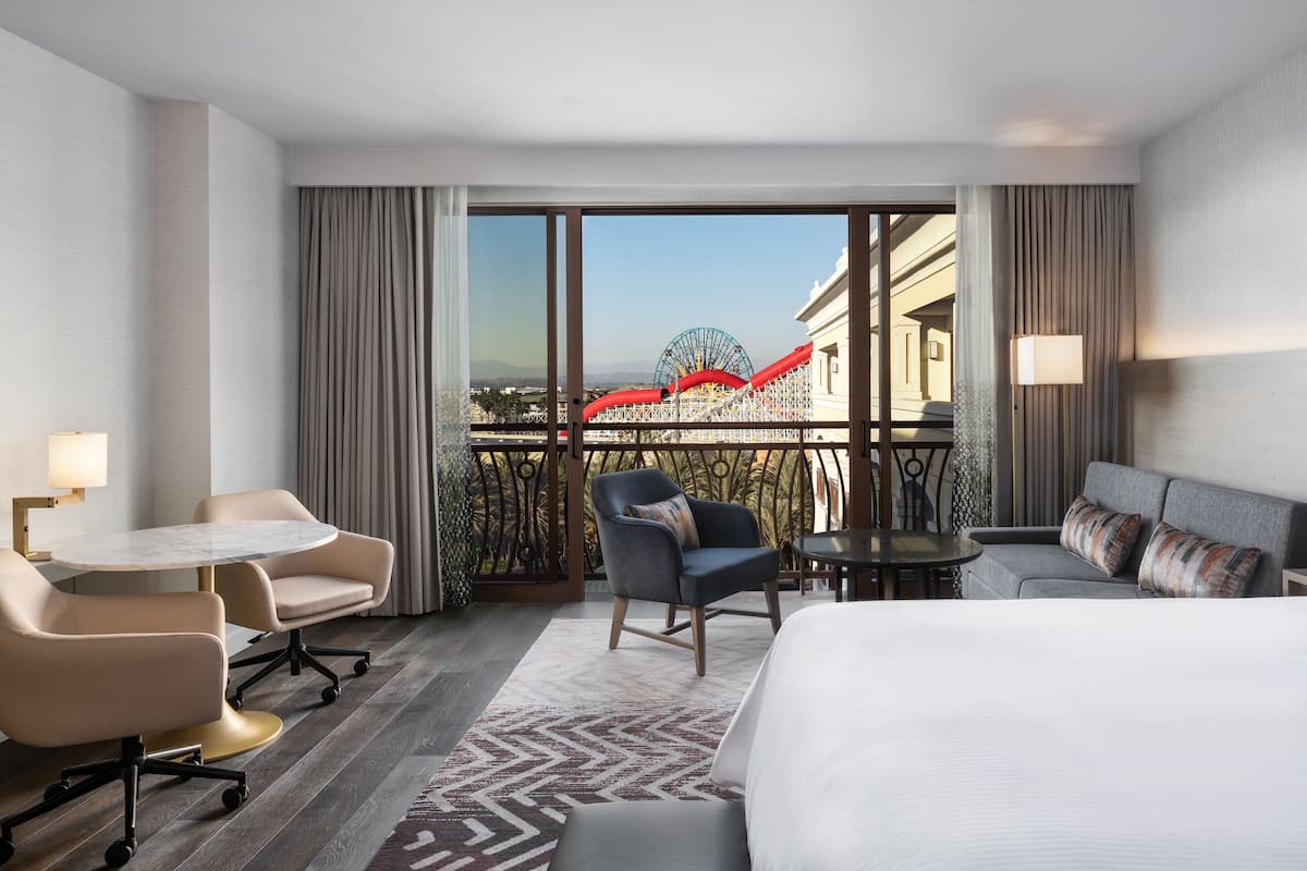Habitación de hotel con cama, escritorio, dos sillones, sofá y vista a una noria.