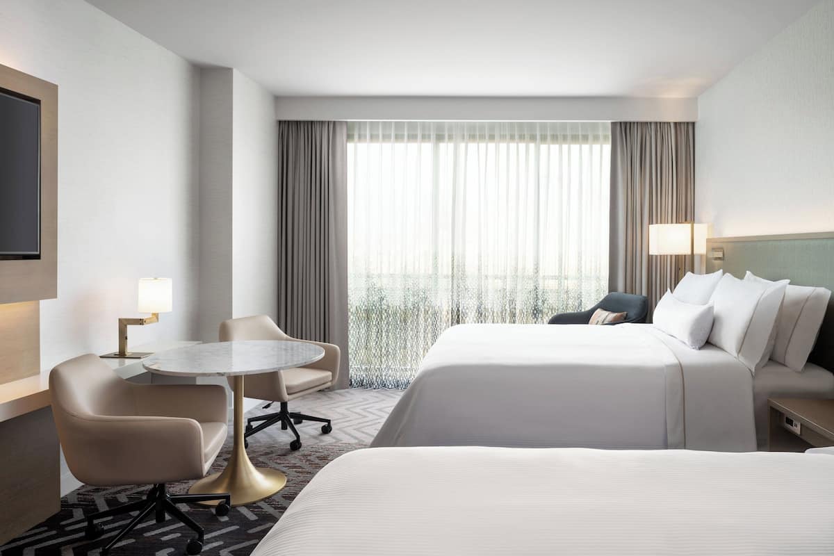 Habitación de hotel con cama, escritorio, silla y ventana con cortinas.