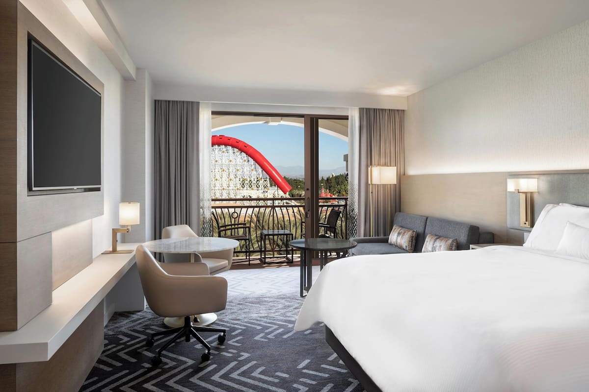 Habitación de hotel con una cama grande, un escritorio con silla, una mesita y un balcón con una estructura roja.