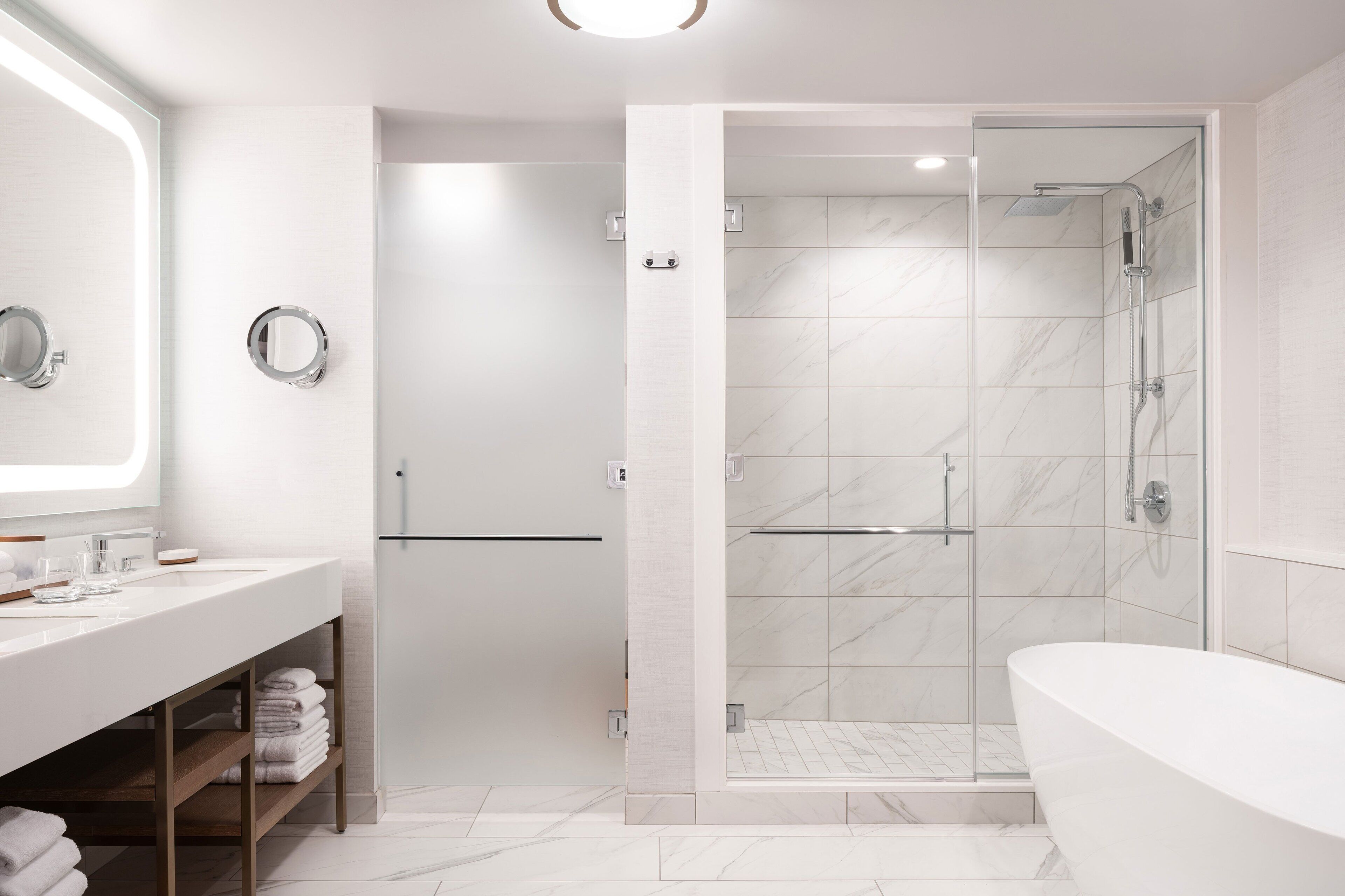 A modern bathroom with a large mirror, a white sink, a shower with glass doors, and a freestanding bathtub.