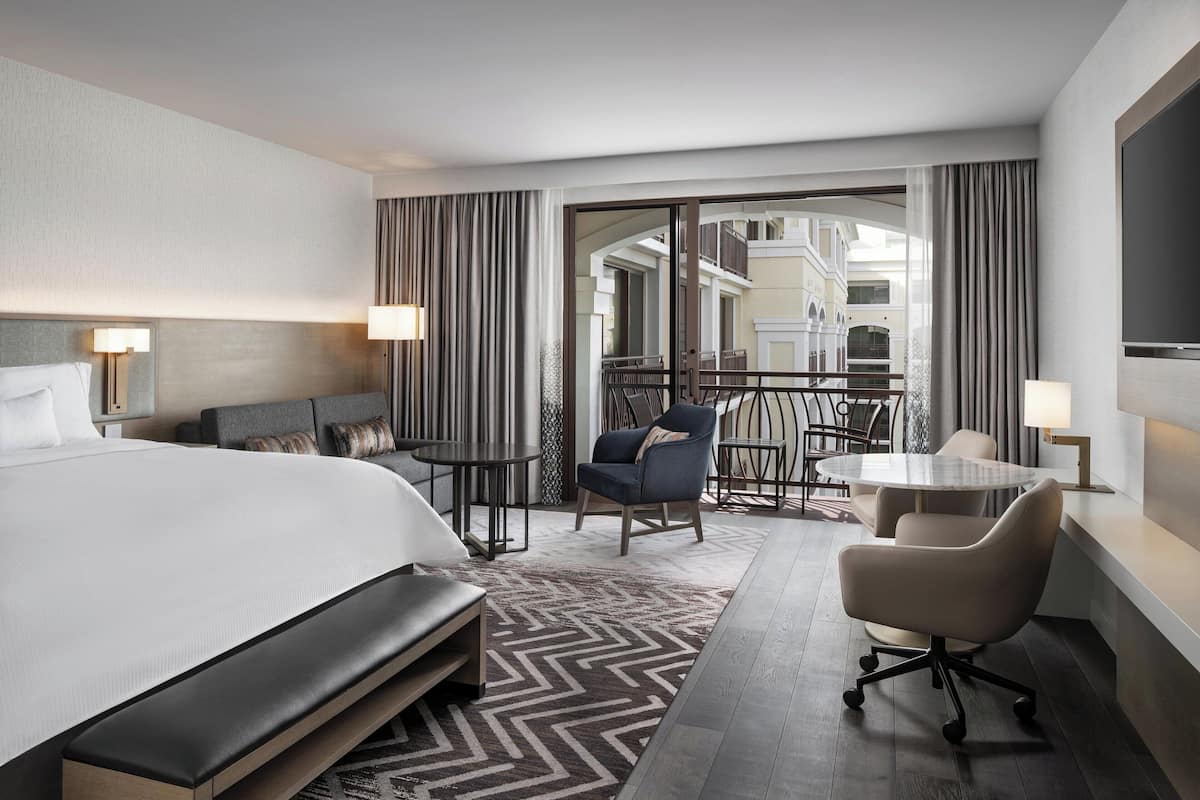Una habitación de hotel moderna con una cama grande, un escritorio, una silla y un balcón con vistas a la ciudad.