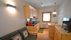 A compact living space with a kitchenette, a sofa with decorative pillows, a wooden dining table, and a television. - Cosy apartment for 3 guests with WIFI, TV, patio and pets allowed (Raveo)