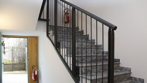 A staircase with black railings and marble steps, a fire extinguisher mounted on the wall, and a door leading outside. - Cosy apartment for 3 guests with WIFI, TV, patio and pets allowed (Raveo)