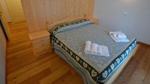 A bedroom with a wooden headboard, a bed with patterned bedding, and a set of towels on the bed. - Beautiful apartment for 3 guests with WIFI, TV, patio and pets allowed (Raveo)