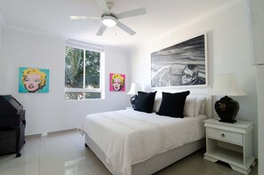 Une chambre à coucher comprenant un lit, une table de chevet, un ventilateur de plafond et deux fenêtres.
