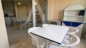 A small, open-plan living area with a dining table and chairs, a kitchenette, and a sliding glass door leading to a balcony. - 1 CHAMBRE, DERNIER ETAGE AVEC ASC, CLIMATISATION (Sète)