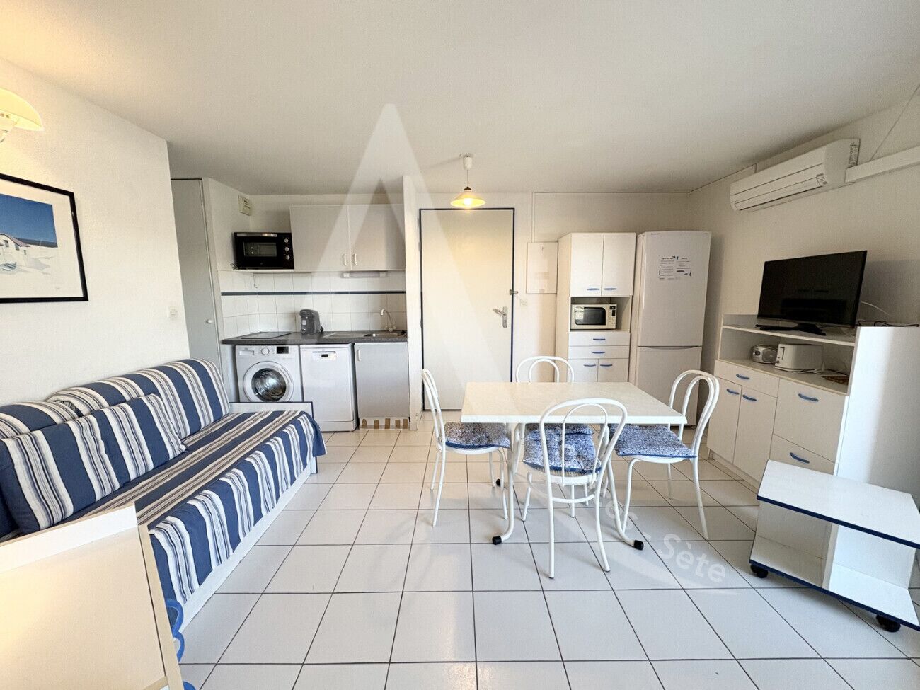 A compact kitchen with a dining area, a sofa, and a television.