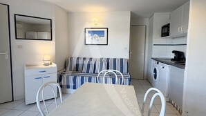 A compact living space with a dining table, a sofa, a small kitchen area with a microwave and washing machine, and a mirror on the wall. - 1 CHAMBRE, DERNIER ETAGE AVEC ASC, CLIMATISATION (Sète)