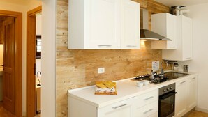 A modern kitchen with white cabinetry, a wooden backsplash, and a gas stove. - Cosy apartment for 2 people with WIFI, TV and patio (Raveo)