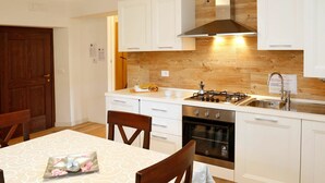 A modern kitchen with white cabinets, a stainless steel stove, and a wooden backsplash. - Cosy apartment for 2 people with WIFI, TV and patio (Raveo)