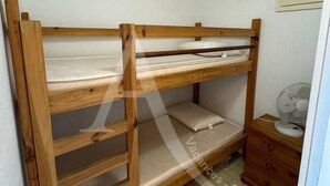 A bunk bed with a wooden frame, a small bedside table, and a fan. - STUDIO 4 PERS AVEC PKG BORD DE PLAGE VUE MER (Sète)