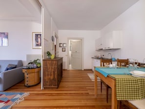 A compact living space with a sofa, a wooden sideboard, a dining table with a checkered tablecloth, and a kitchen area with cabinets and a stove.