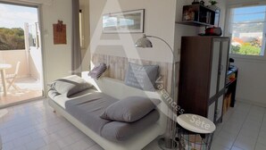 A modern bedroom with a bed, a desk, and a chair. There is a window with a view of trees and a balcony.